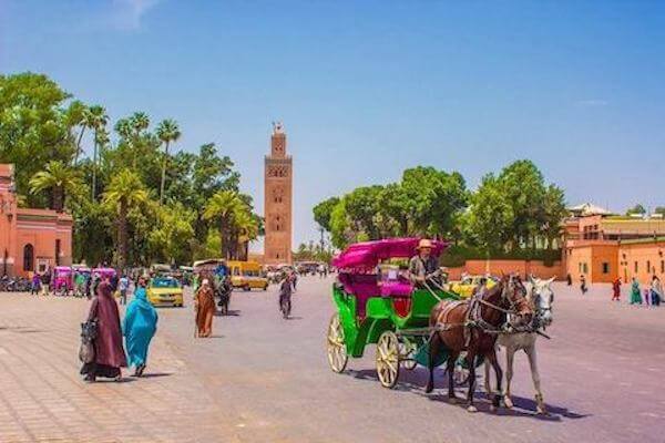 Tourists exploring the lively streets of Marrakech, surrounded by colorful souks, street performers, and historic landmarks.