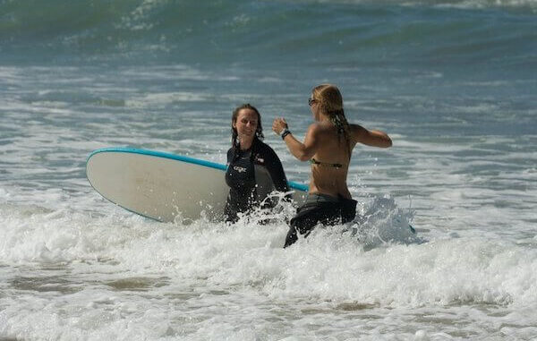 Surf instructor helping young child balance on surfboard in shallow water